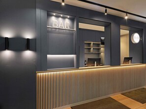 Un comptoir d’accueil moderne avec une enseigne « BAR », un espace d’accueil avec des étagères et une enseigne « B&B HOTELS ».