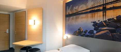 A hotel room with a bed, a desk, and a wall-mounted light.