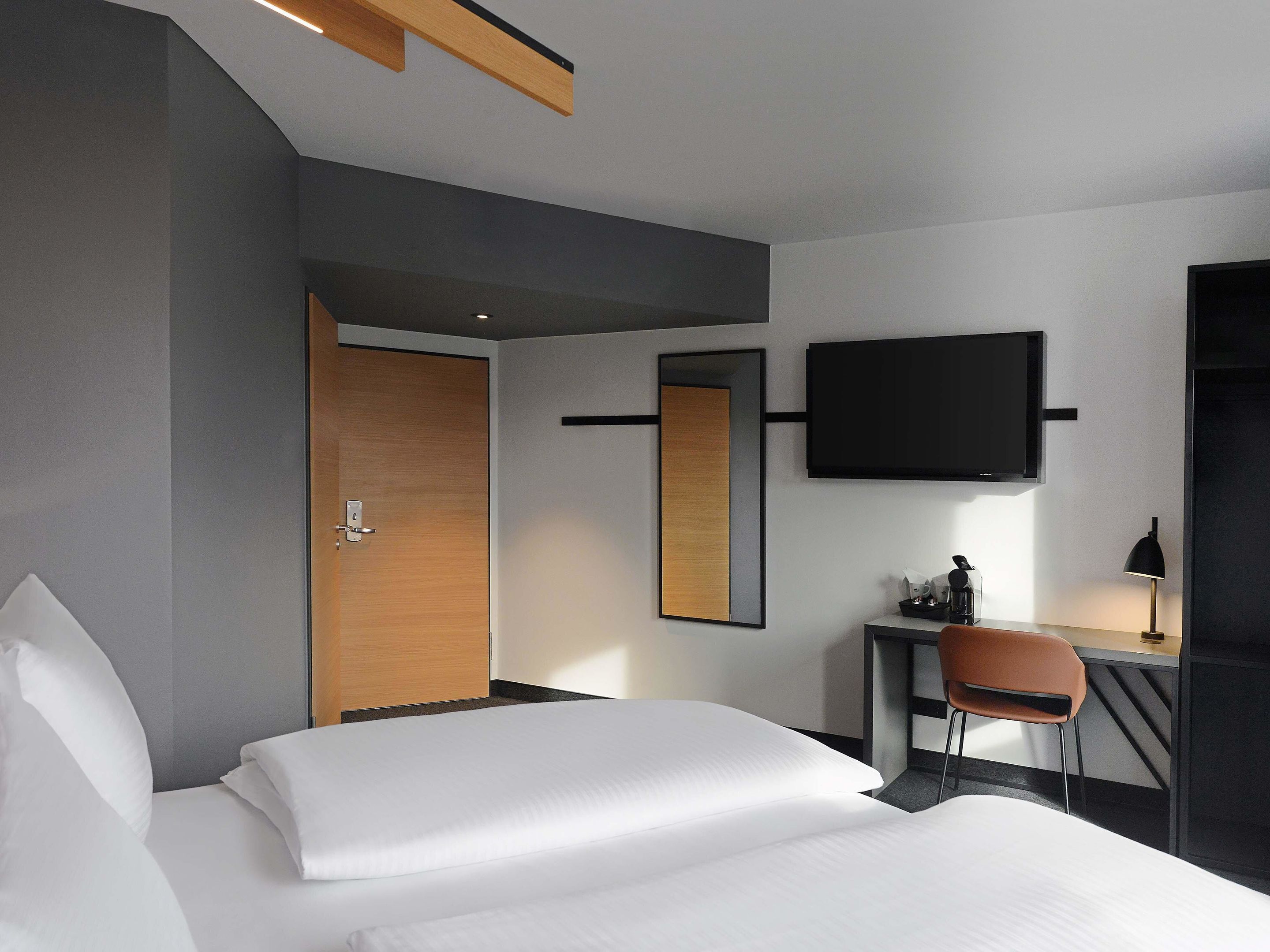 Une chambre d’hôtel avec un lit, un bureau, une chaise, une télévision et une porte.