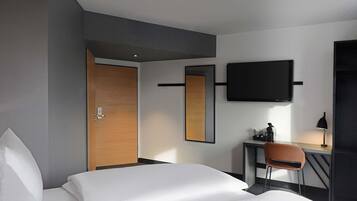 Une chambre d’hôtel avec un lit, un bureau, une chaise, une télévision et une porte.