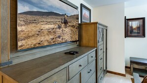 Ett rum med en stor TV som visar ett landskapsmotiv, ett träskåp och en inramad tavla på väggen.