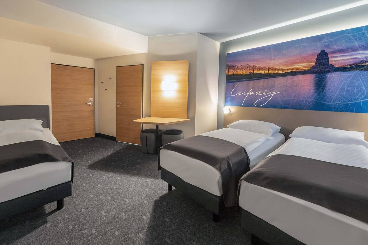 A hotel room with two single beds, a double bed, a small table, and a wall-mounted TV.