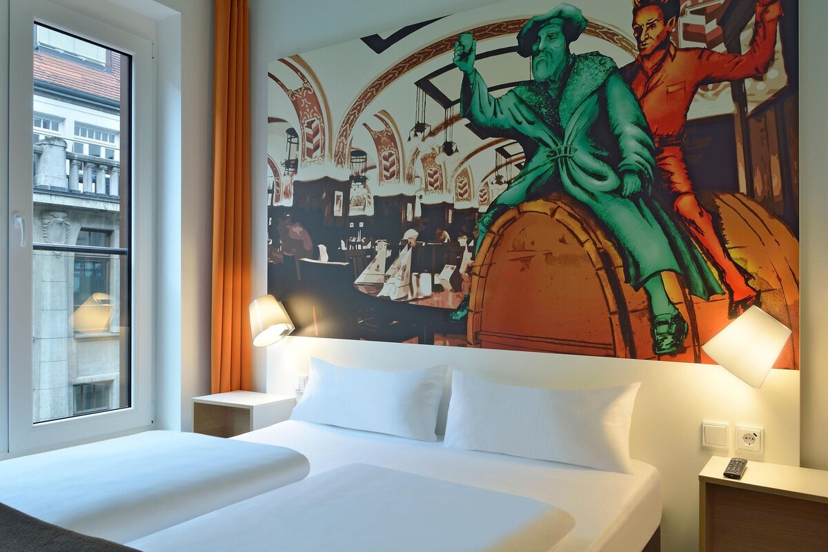 Una habitación de hotel con una cama grande, una ventana con cortinas y un mural en la pared.