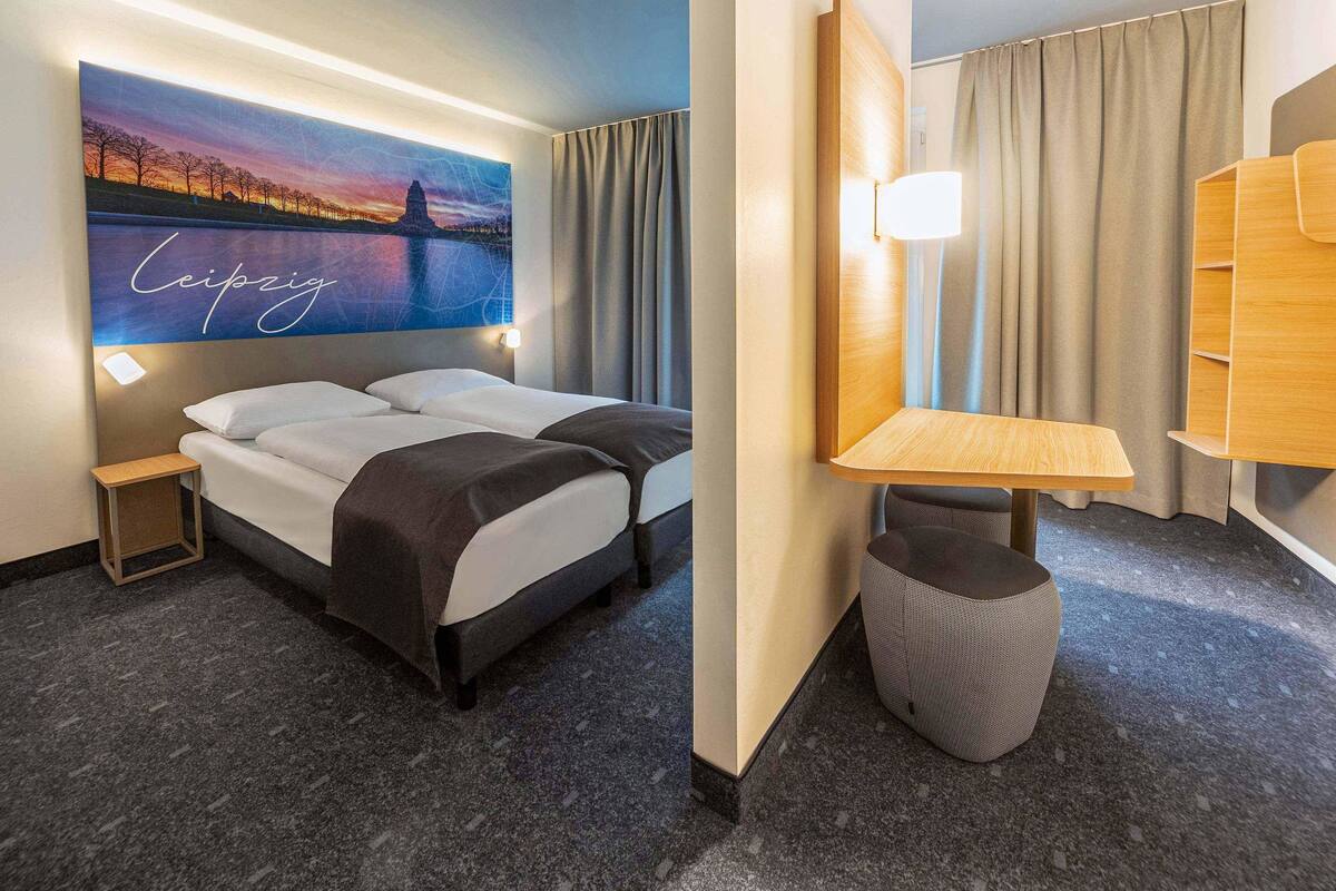A hotel room with a bed, a nightstand, a desk, and a large wall mural.