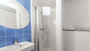 Ein Badezimmer mit einem weißen Waschbecken, blautonierten Fliesen, einer Duschkabine und einem weißen Handtuch an der Wand.