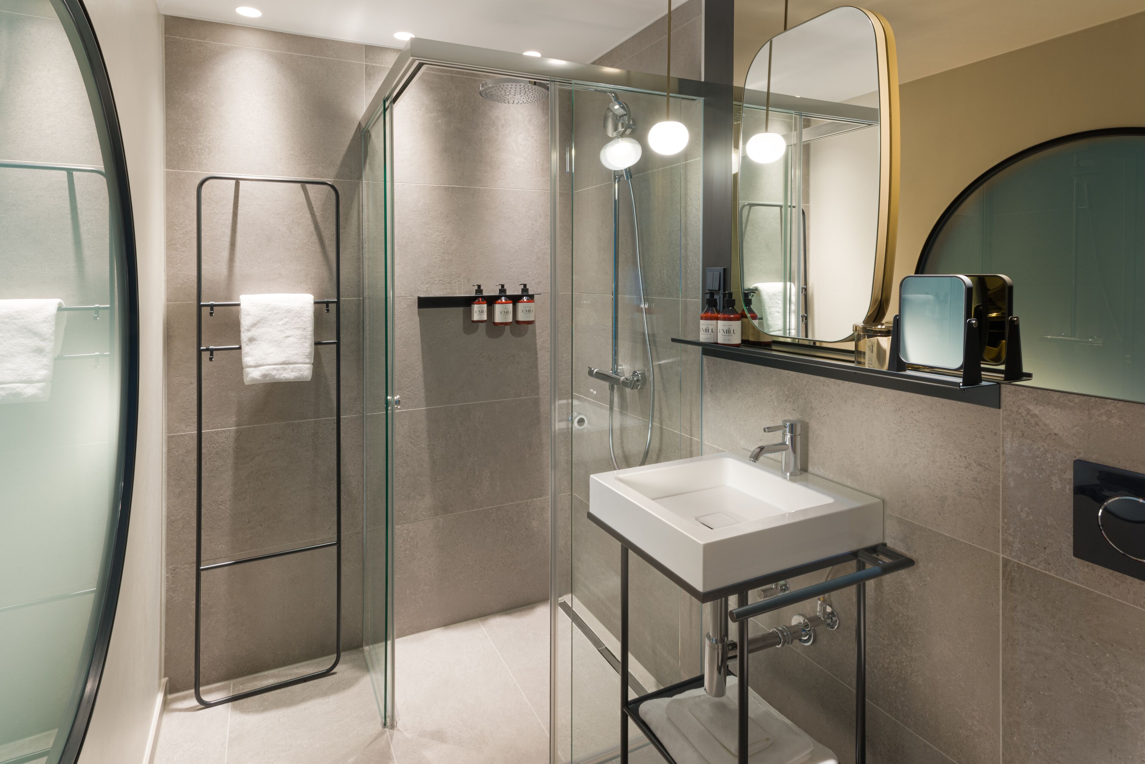 Un baño moderno con ducha de vidrio, lavamanos blanco y un espejo grande.
