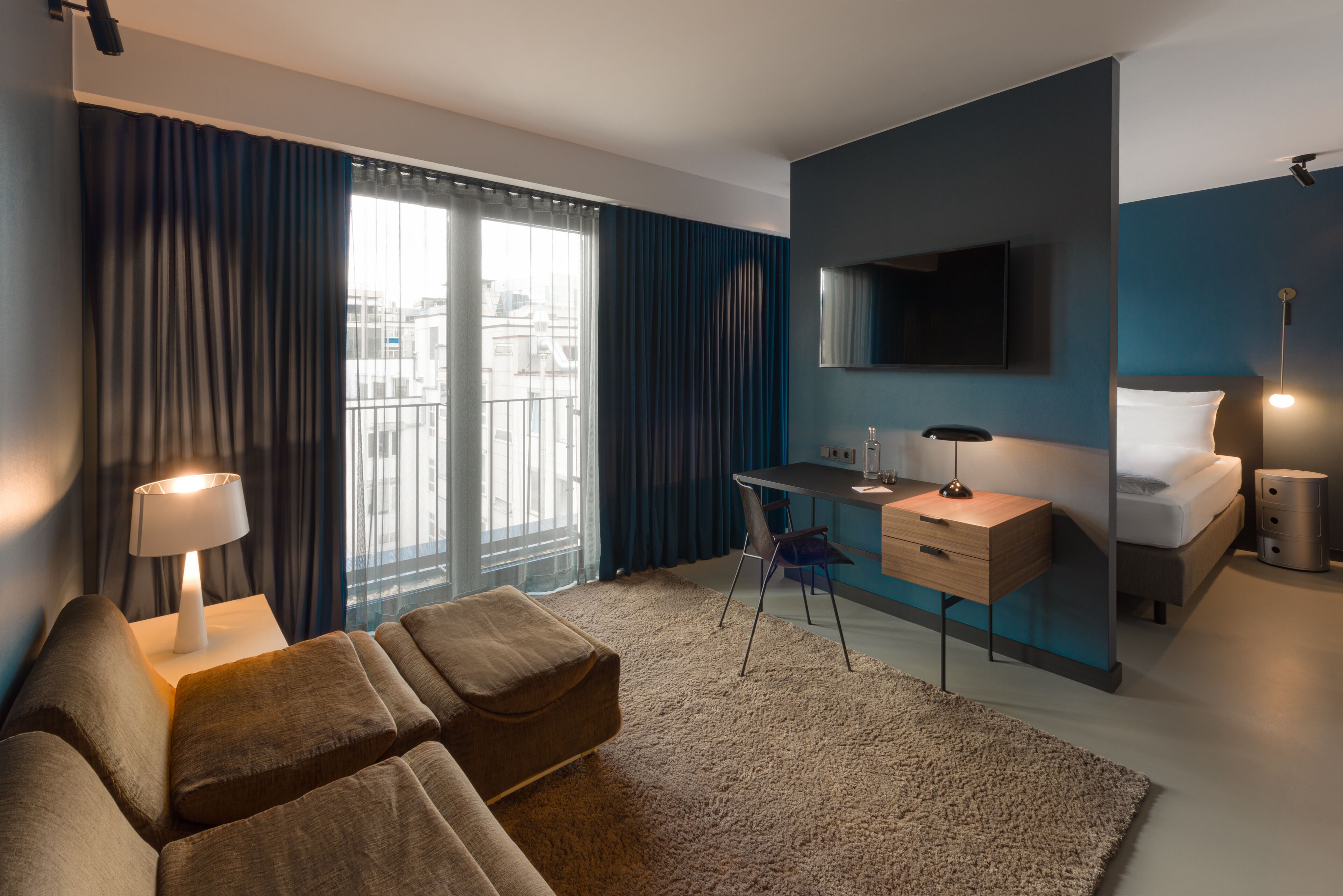 Una habitación de hotel moderna con una cama, un escritorio, una silla y un televisor instalado en la pared.