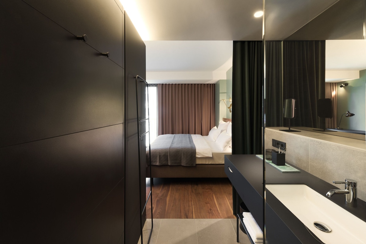 Una habitación de hotel moderna con cama, un espejo grande, un lavamanos y un armario oscuro.