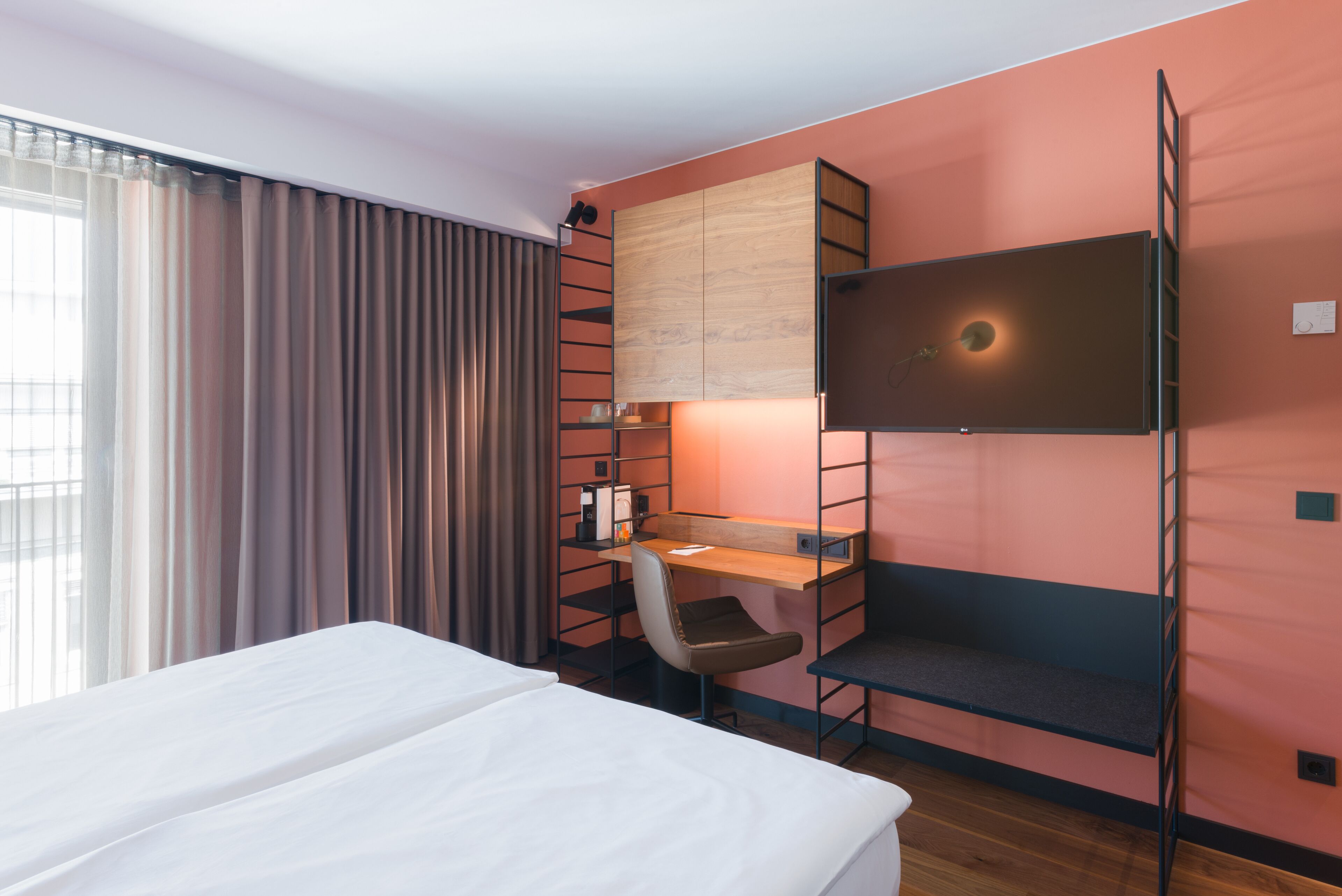 A hotel room with a bed, a desk, a chair, a TV, and a wardrobe.