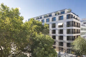 A modern multi-story building with large windows and balconies, surrounded by trees.