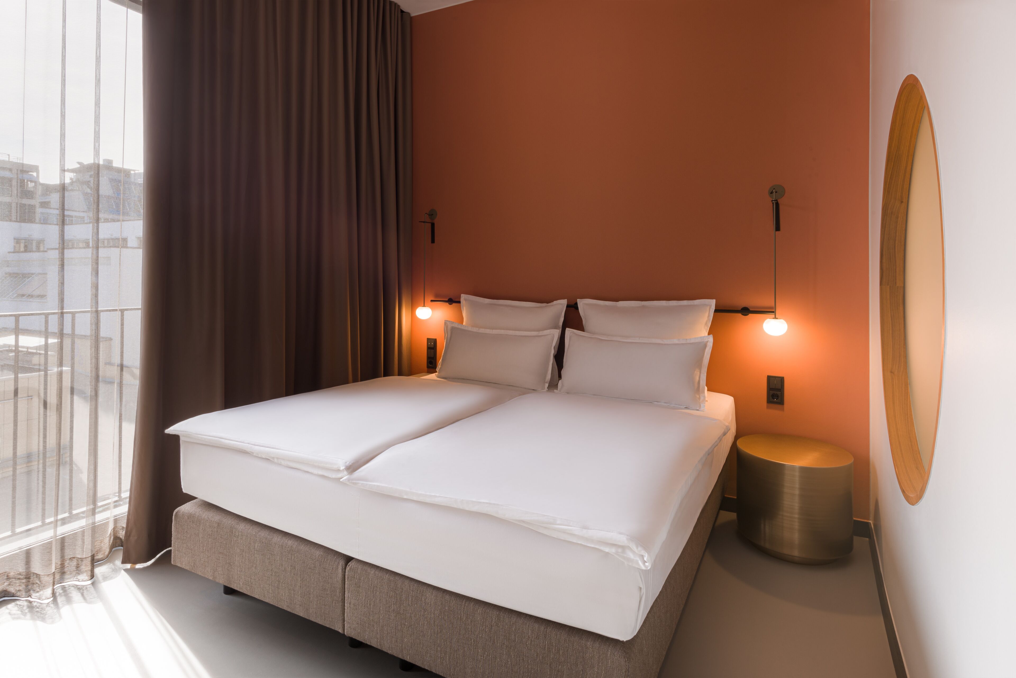 Camera d'albergo con un letto grande, due comodini, un tavolino rotondo e un'ampia finestra con tende.