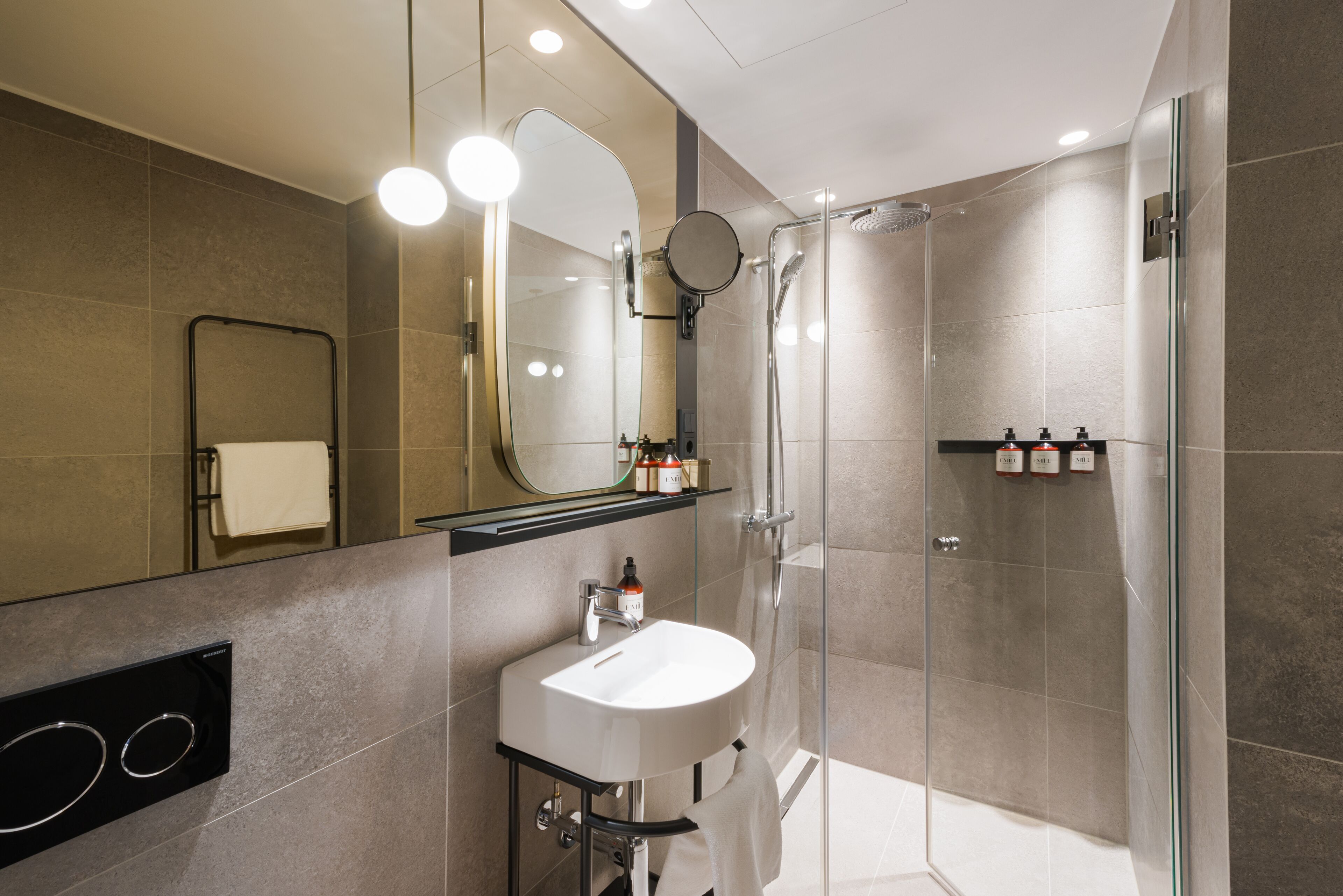 Ein modernes Badezimmer mit einer Glaskabine zur Dusche, einem weißen Waschbecken und einem Spiegel mit Beleuchtung darüber.