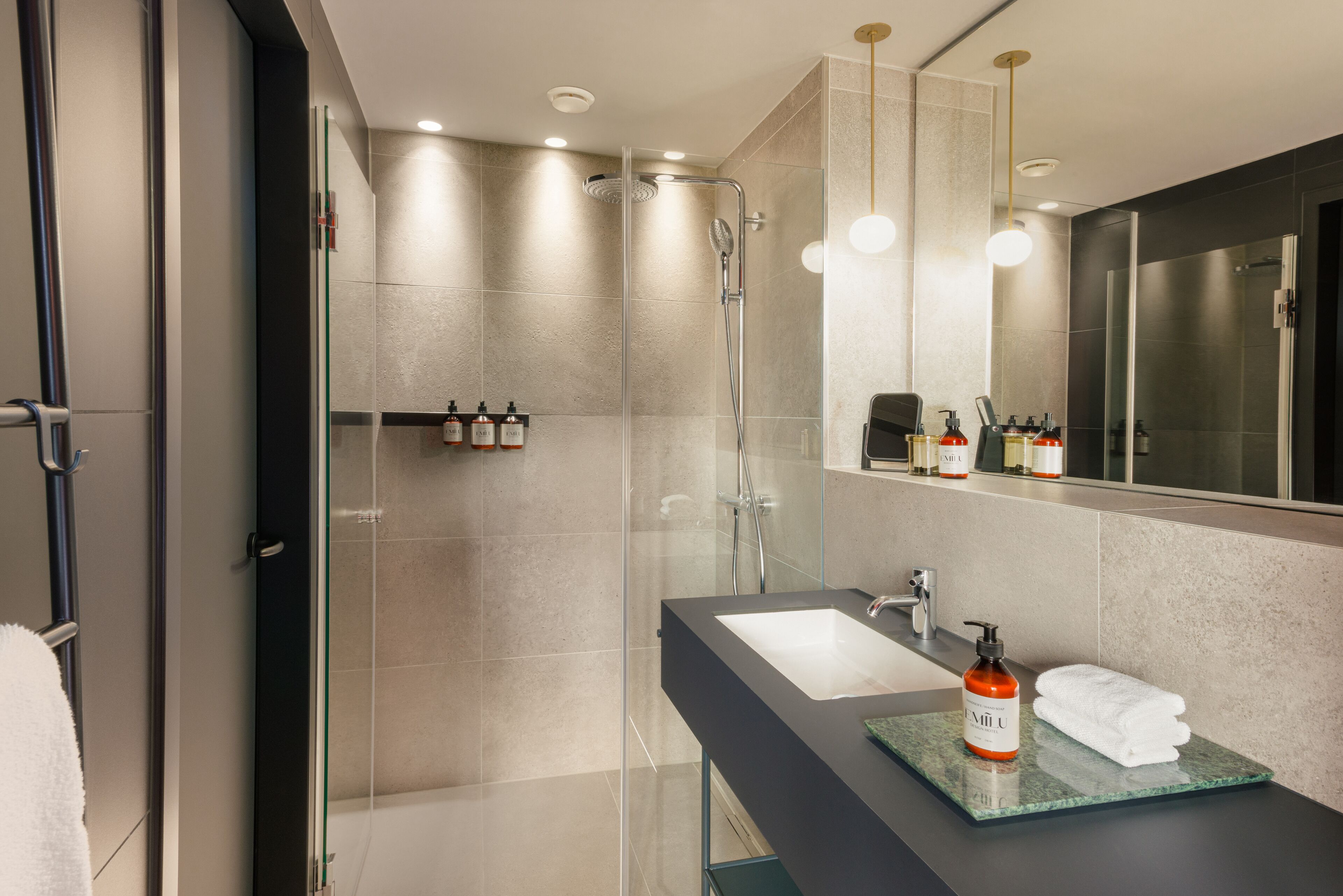 Une salle de bain moderne dotée d’une douche à parois de verre, d’un grand miroir et d’un meuble-lavabo avec un évier et un porte-serviettes.