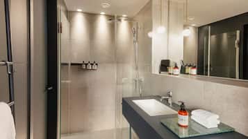 Une salle de bain moderne dotée d’une douche à parois de verre, d’un grand miroir et d’un meuble-lavabo avec un évier et un porte-serviettes.
