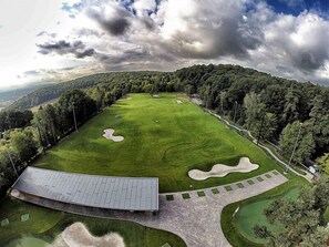 A golf course with a clubhouse, surrounded by dense forest.