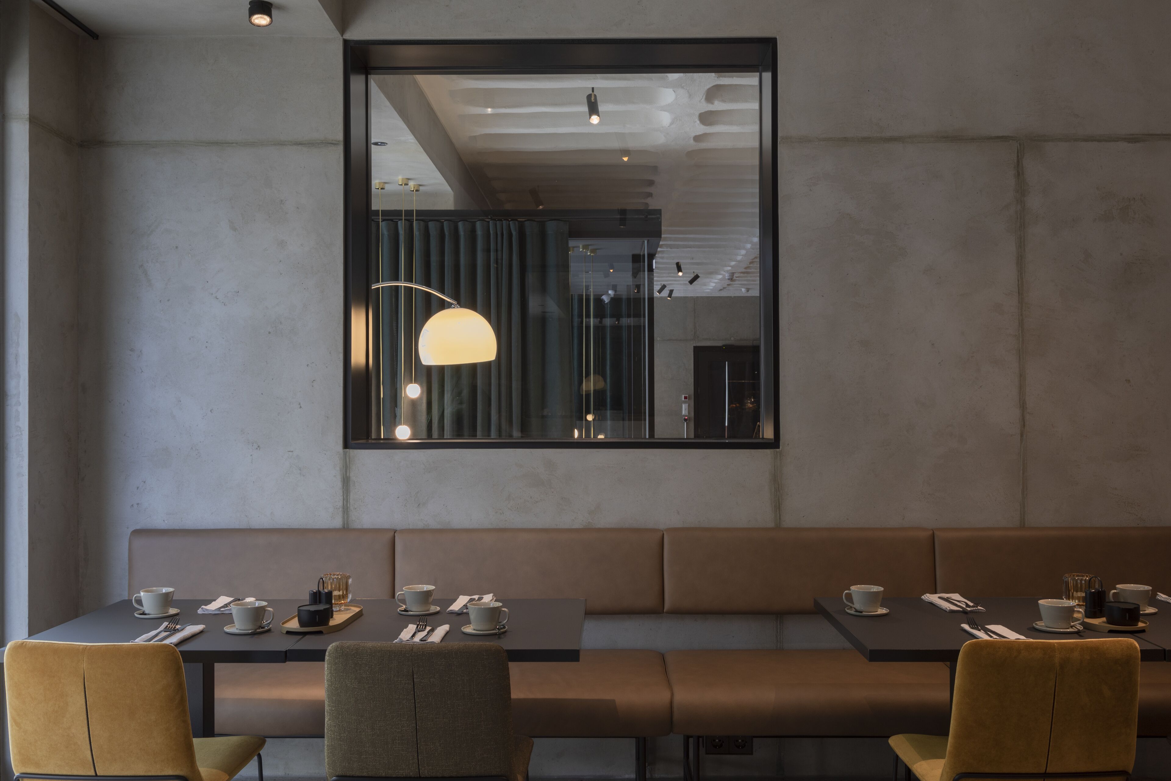 A modern restaurant interior with a long bench seating area, tables with dining ware, and pendant lighting.
