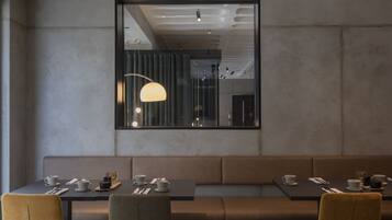A modern restaurant interior with a long bench seating area, tables with dining ware, and pendant lighting.