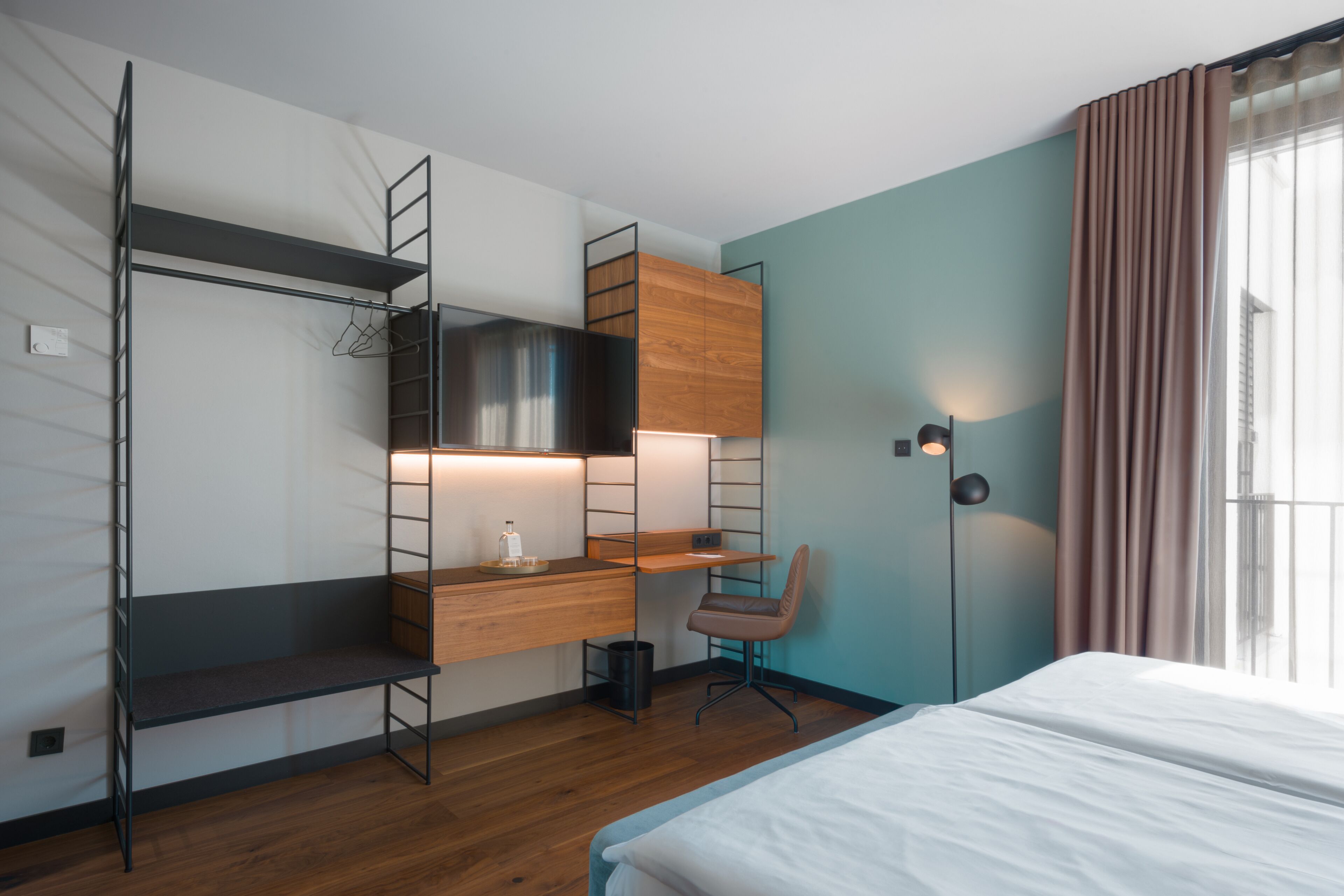 A compact hotel room with a bunk bed, a desk with a chair, a wardrobe, and a bedside table.