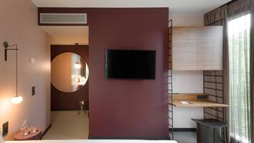 Una habitación de hotel moderna con una cama grande, un televisor de pantalla plana en la pared, un escritorio pequeño con una silla y una ventana con cortinas.