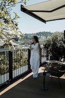 Un balcón con vista a un paisaje urbano, una mesa con una tetera y una silla.