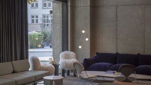 Una sala moderna con sofá, mesa de comedor y una silla. Hay luces colgantes y vistas al exterior.