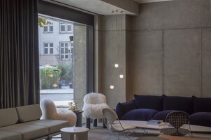 Una sala moderna con sofá, mesa de comedor y una silla. Hay luces colgantes y vistas al exterior.