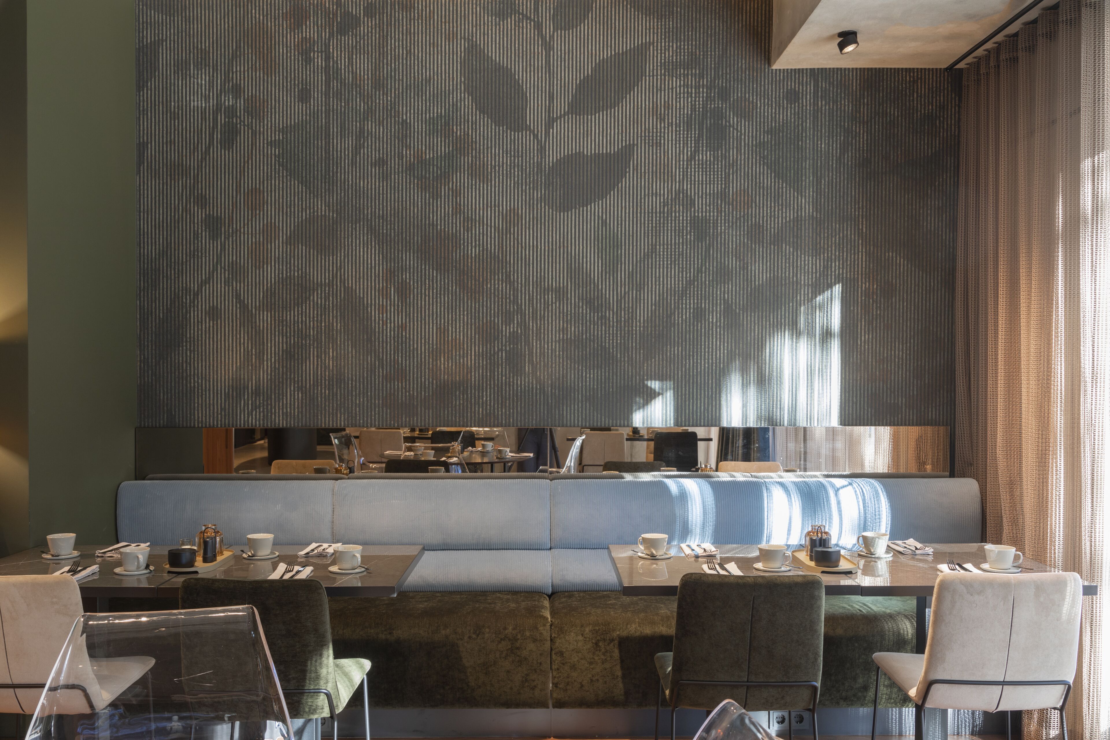 A modern dining area with a long table, cushioned seating, and a large decorative wall.