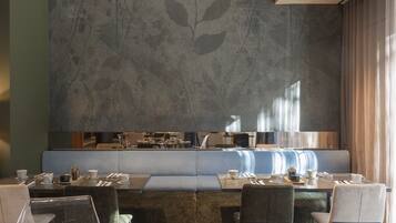 A modern dining area with a long table, cushioned seating, and a large decorative wall.