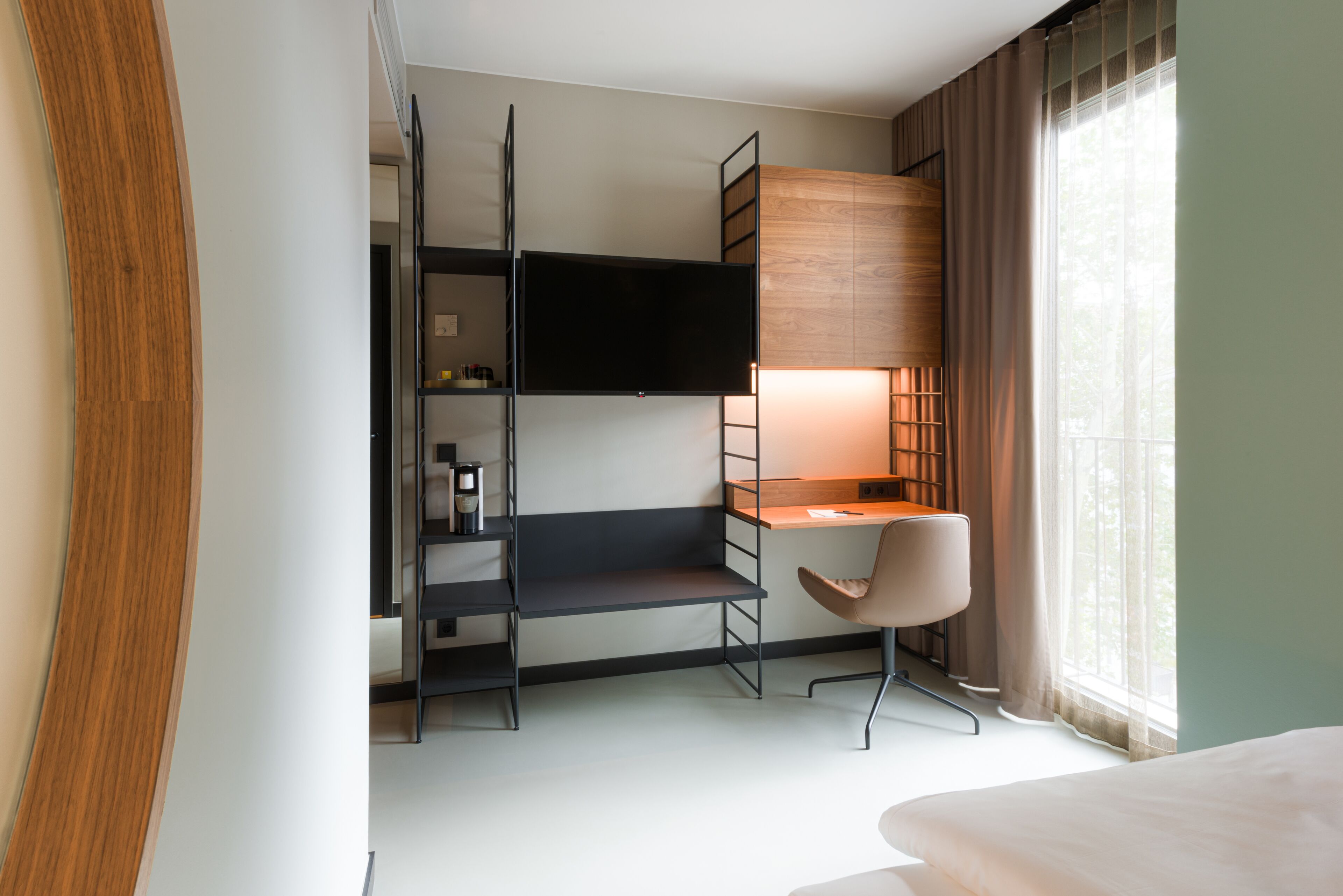 A compact hotel room with a bunk bed, a desk with a chair, a TV mounted on the wall, and a window with curtains.