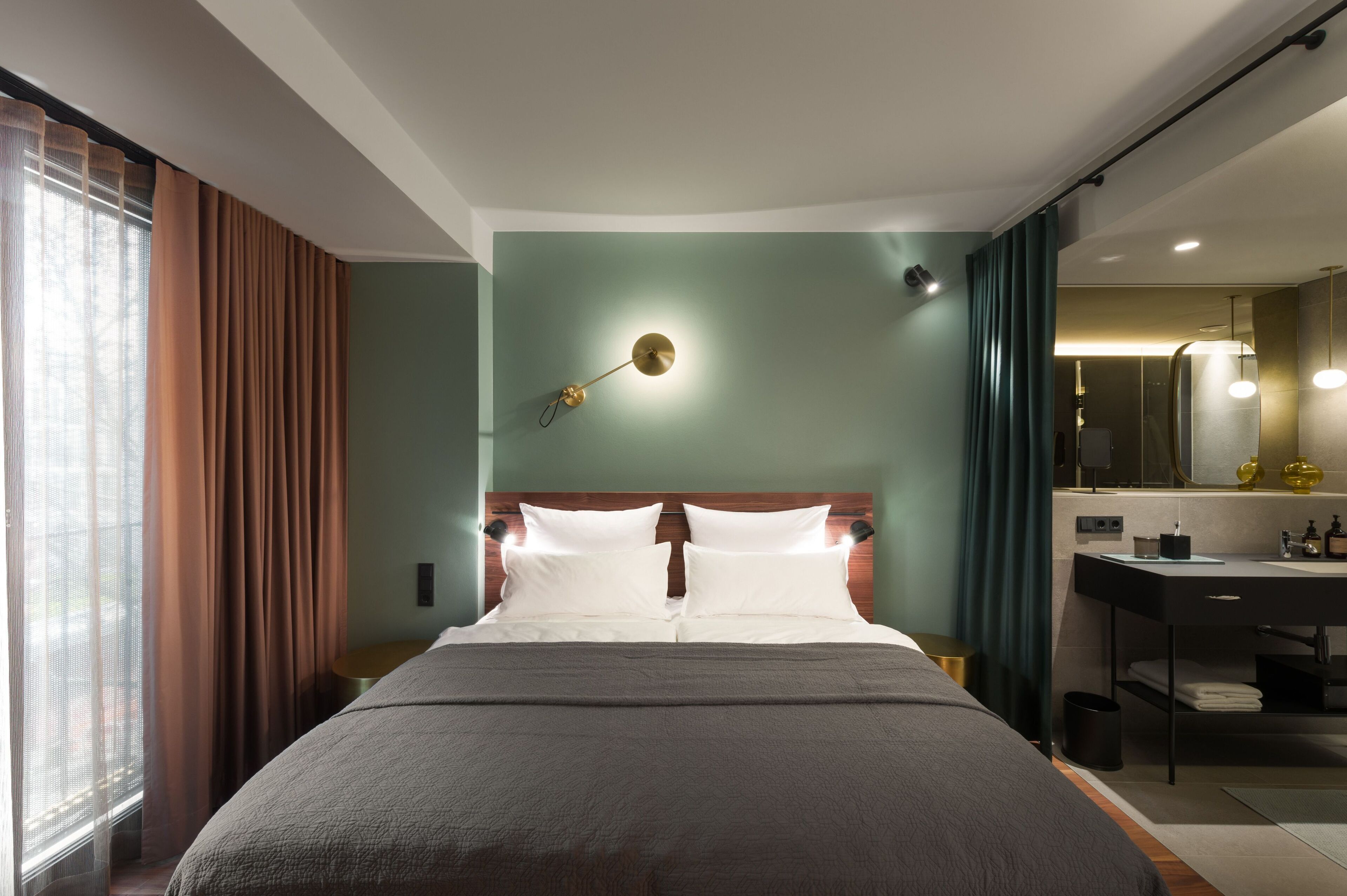 Une chambre d’hôtel moderne dotée d’un grand lit, d’une table de chevet, d’un miroir et d’une salle de bain avec un lavabo et une douche.