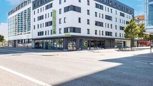 Un hôtel moderne à la façade blanche, doté de plusieurs étages et d’un hall d’accueil spacieux et bien visible.