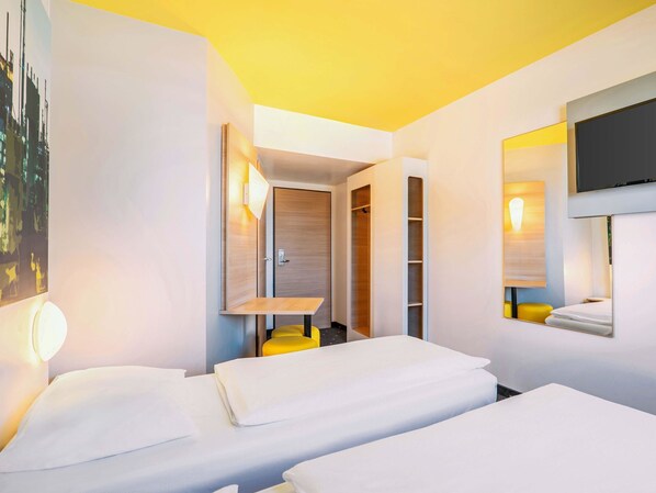Habitació d'hotel amb dos llits, un televisor, un mirall i un armari.