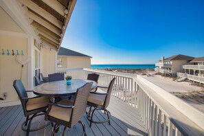 A deck with a round table and wicker chairs, overlooking a beach.