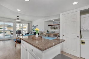 A modern kitchen with granite countertops, a dining area with a wooden table and chairs, and a view through large sliding glass doors to an outdoor balcony.