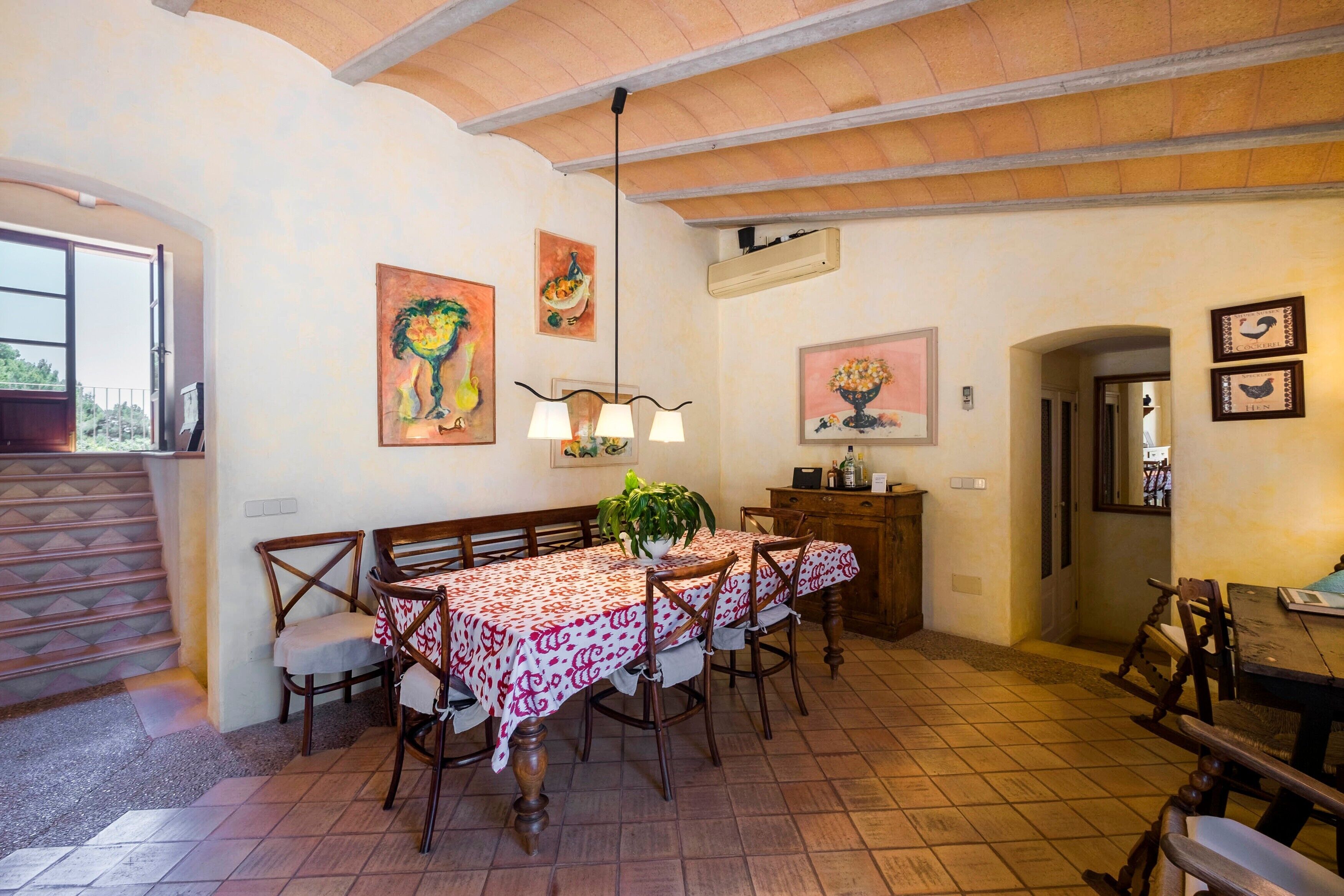 A dining area with a table set for four, wooden chairs, a potted plant, and artwork on the walls.