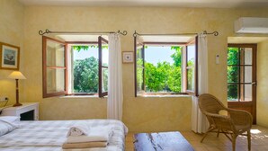 A room with two open windows, a bed with a checkered bedspread, a chair, and a wooden table. - Natural Stone Villa with Pool: Villa Son Reus (Felanitx)