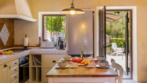 A kitchen with a dining table, white cabinets, a built-in oven, a coffee machine, and a window with a view of greenery. - Natural Stone Villa with Pool: Villa Son Reus (Felanitx)