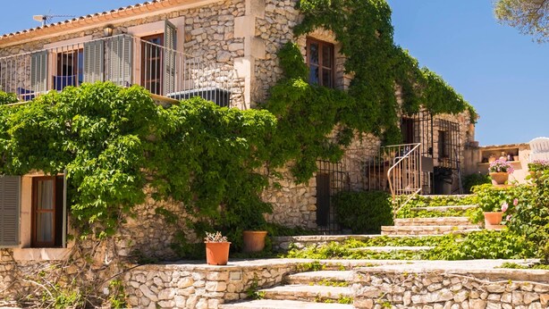 A stone building with a stone staircase, a small garden, and a clear blue sky. - Natural Stone Villa with Pool: Villa Son Reus (Felanitx)