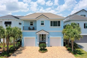 A two-story house with a front entrance, a garage, and a small front yard with palm trees.