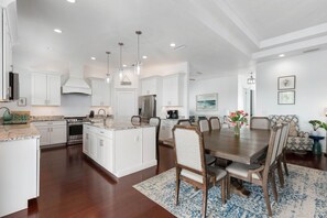 A spacious kitchen with white cabinetry, a central island, and a dining area with a wooden table and chairs.