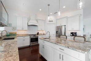 A modern kitchen with white cabinetry, stainless steel appliances, granite countertops, and pendant lighting.
