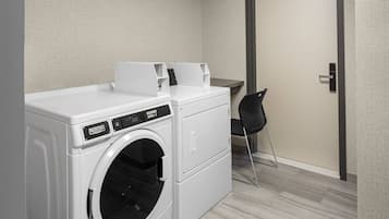 A compact laundry area with a front-loading washing machine, a dryer, and a small folding table.