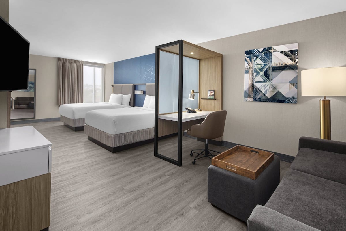 Une chambre d’hôtel avec deux lits, un bureau, une chaise, un canapé et une télévision.