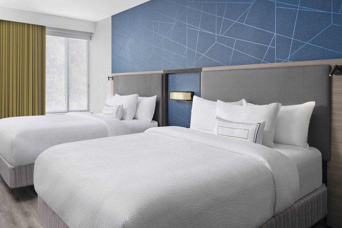 Une chambre d’hôtel avec deux lits, une grande fenêtre avec des rideaux et un mur orné d’un motif géométrique.