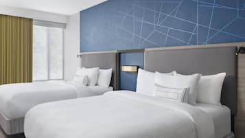 A hotel room with two beds, a large window with curtains, and a geometric-patterned wall.