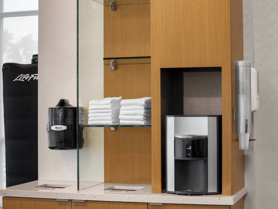 A modern bathroom with a glass partition, a coffee machine, and neatly folded towels.