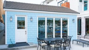 A small, light blue house with a tiled exterior, a front door, and a patio with a table and chairs.
