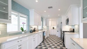 A modern kitchen with white cabinets, a checkered floor, and a window with a plant.