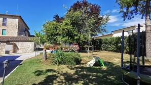 A stone building with a tiled roof, a grassy yard with a slide, and a tree.