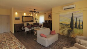 A living room with a sofa, a dining area with a table and chairs, a large mirror, and a painting on the wall.